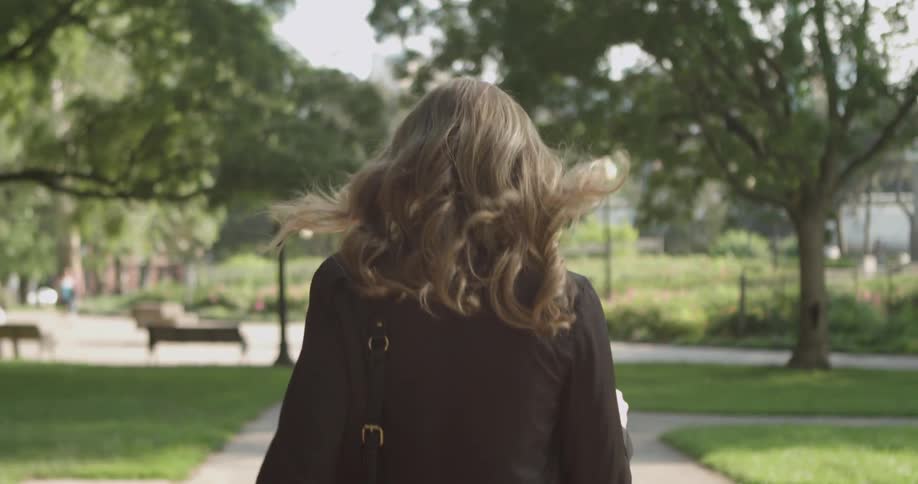 A woman is walking down the sidewalk on a sunny day