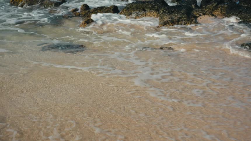 Waves breaking at a beach next to rocks on the sand during day time