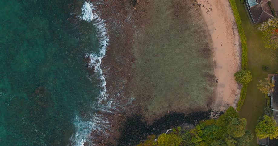 An aerial view of a beach with some waves on the shore and some houses near the sea