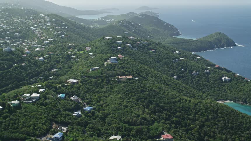 Aerial view of houses and mansions on hills covered with vegetation on an island by the turquoise blue sea
