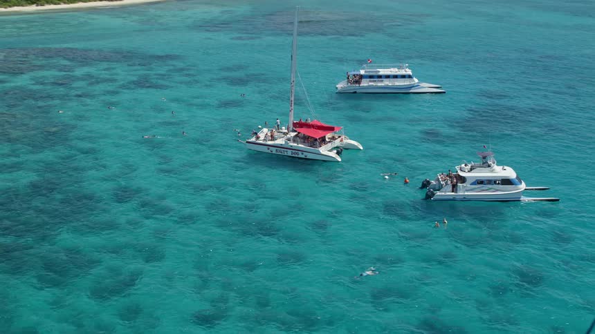 Aerial of people on yachts in the blue sea near a tropical island