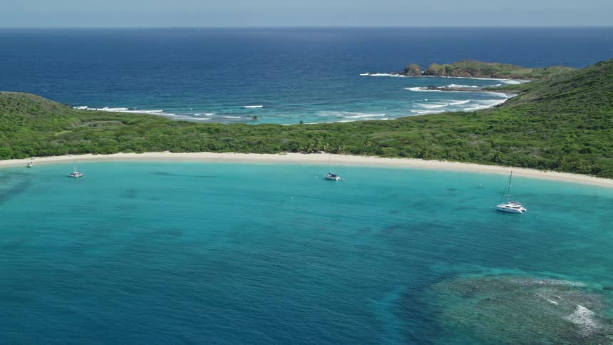 Waves roll past boats onto beach of forested island