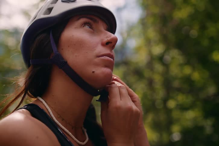 Closeup of a woman adjusting her protective helmet in the midst of a forest