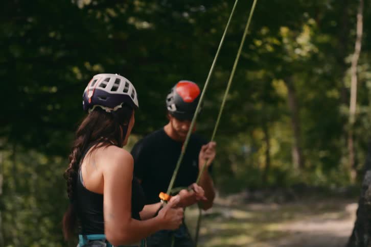 A man on a rope climbs down from a rock and talks to a woman who looks up