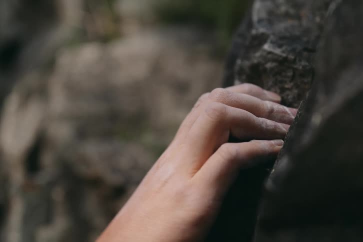 A hand clasping at a rocky cliff face for safety