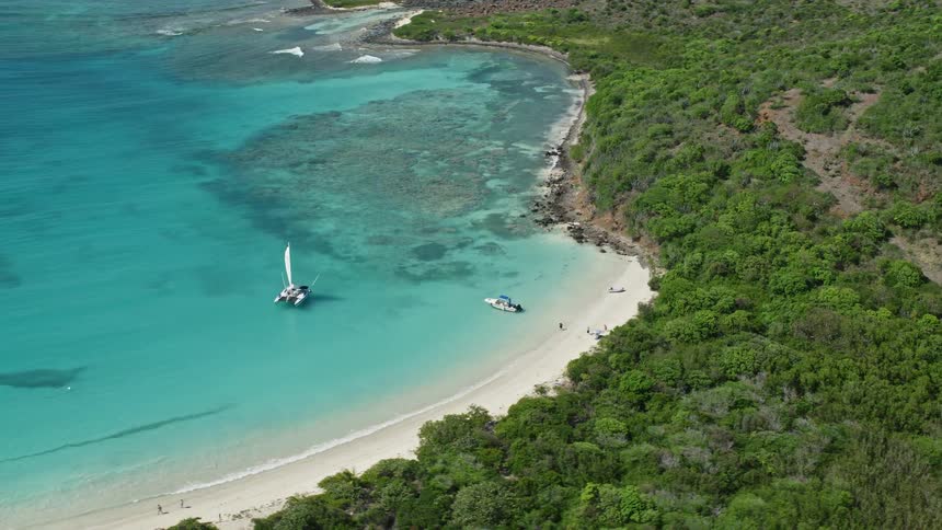 Aerial view of a sailboat and a motorboat on the water next to a beach surrounded by vegetation during day time
