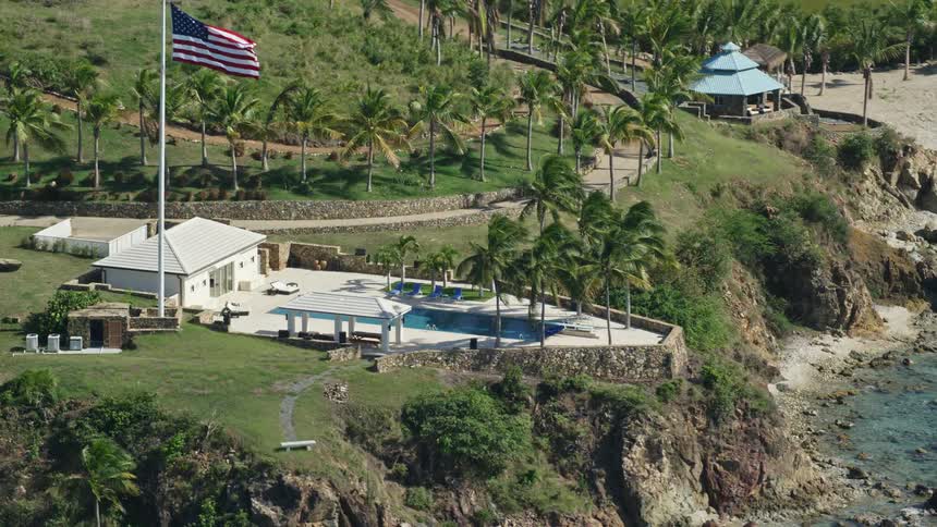 American flag flutters over building with swimming pool in coastal park