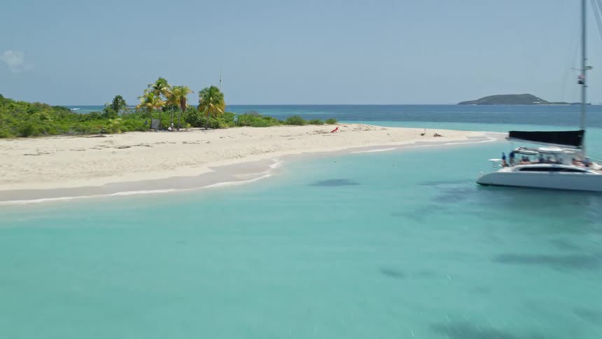 Three sailboats sailing around a tropical island on a clear sea