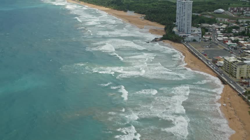 Waves roll onto beach near small coastal city a distance from misty mountains