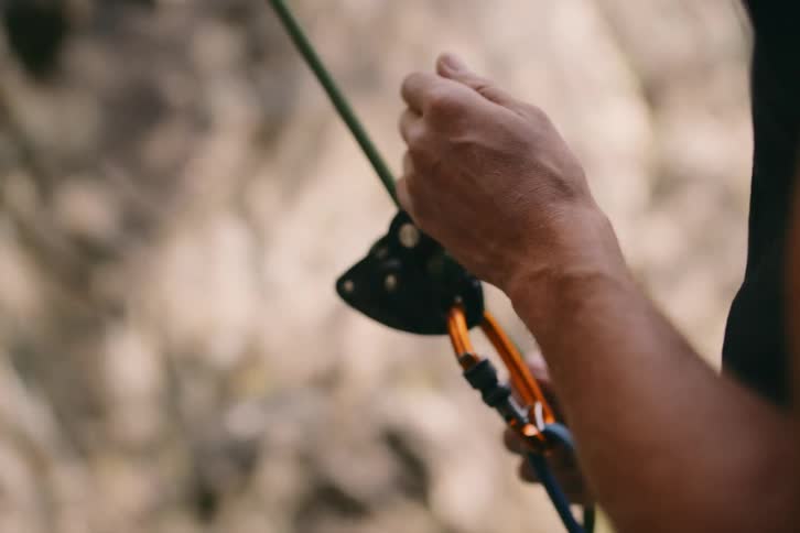 Closeup of a mans hands holding mountain climbing safety equipment with a rope