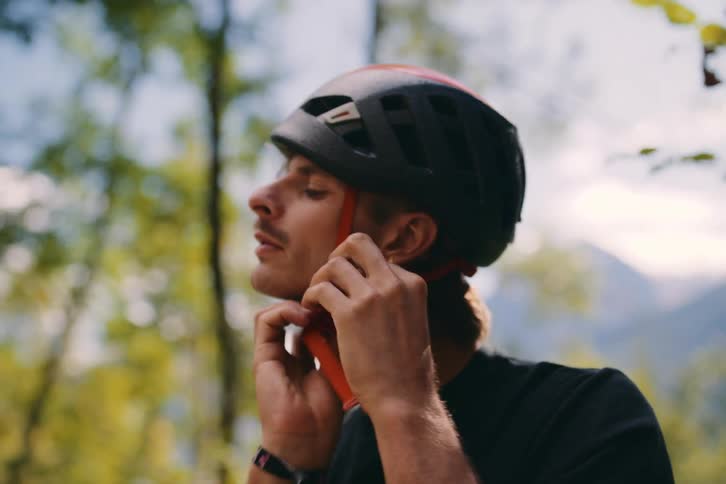 A man in the woods putting on a safety helmet while looking up