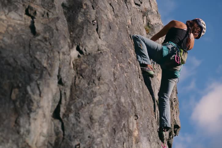A woman is climbing a rock and she is wearing a safety helmet