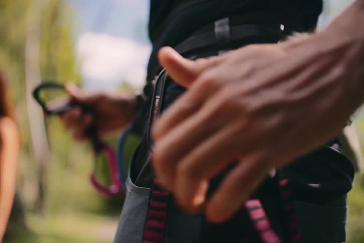 Male climber clips climbing equipment onto harness while woman waits in the background