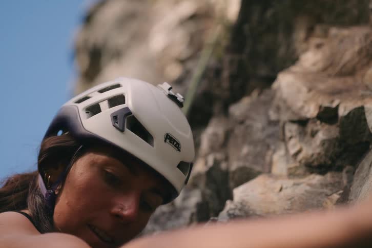 A woman climbing a rocky cliff attached to a safety rope