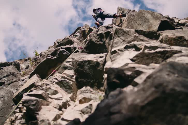 Upward view of a man climbing a rocky mountainous wall