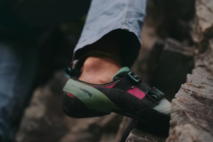 A persons foot wearing shoes stepping on a stone elevated from the ground outdoors during day time