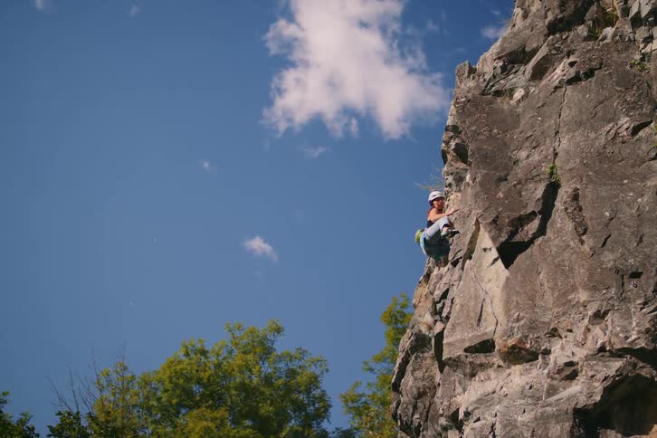 A woman climbs a rocky mountain on a sunny day