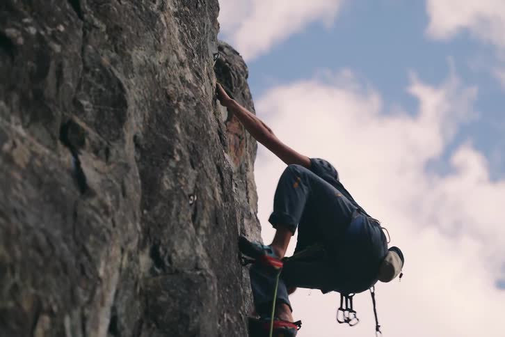 Man wearing a helmet and a black shirt and jeans climbing a rock outdoors during day time