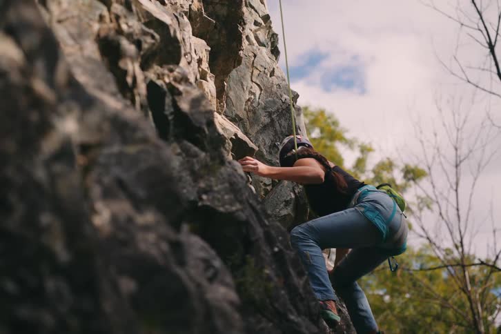 A woman climbing a rocky cliff attached to a safety rope