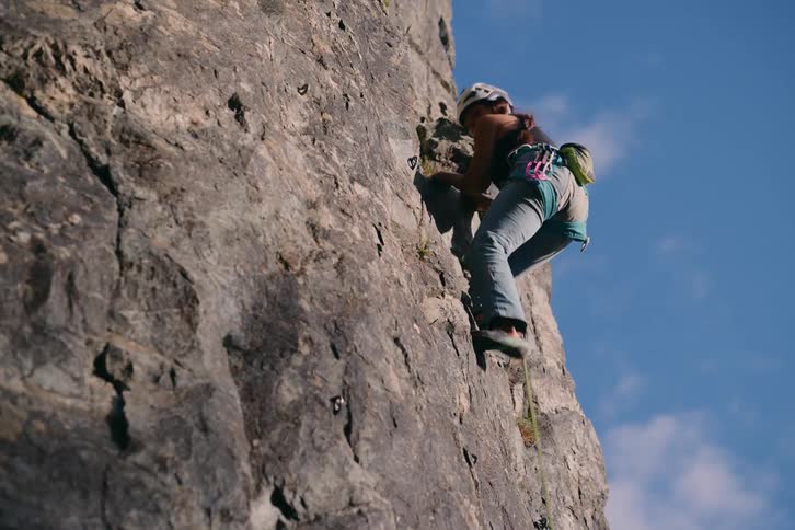 Female rock climber climbs cliff face on cloudy day