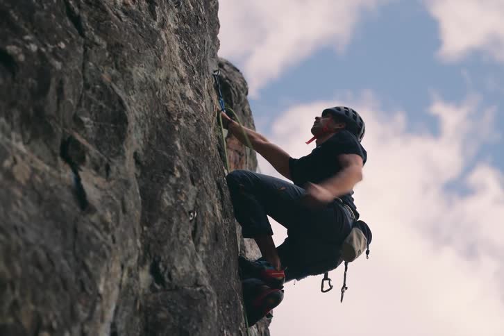 A rock climber looks for hand and foot holds while hanging a safety rope