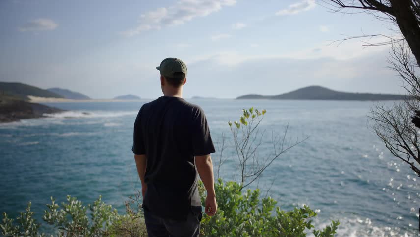 Man on a hill with a view of the blue sea with sunlight reflection