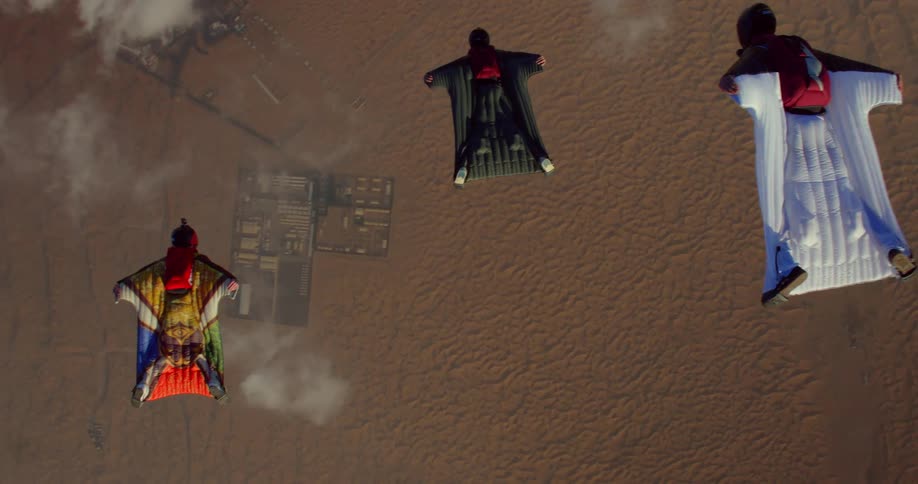 Three people soaring in wingsuits through the air