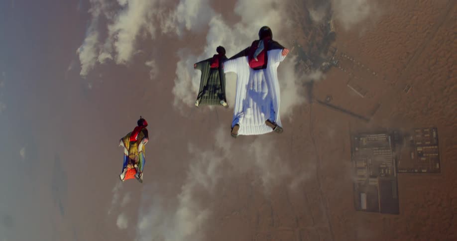 Three people glide wearing wing suits