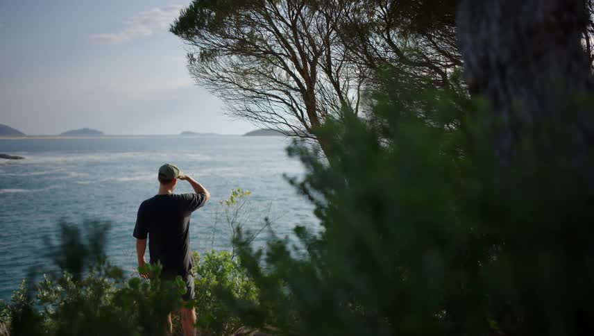 View of a man with his back to the camera on a natural cliff observing the sea