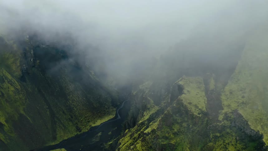Aerial view of a river at the bottom of a valley in the mountains under the clouds