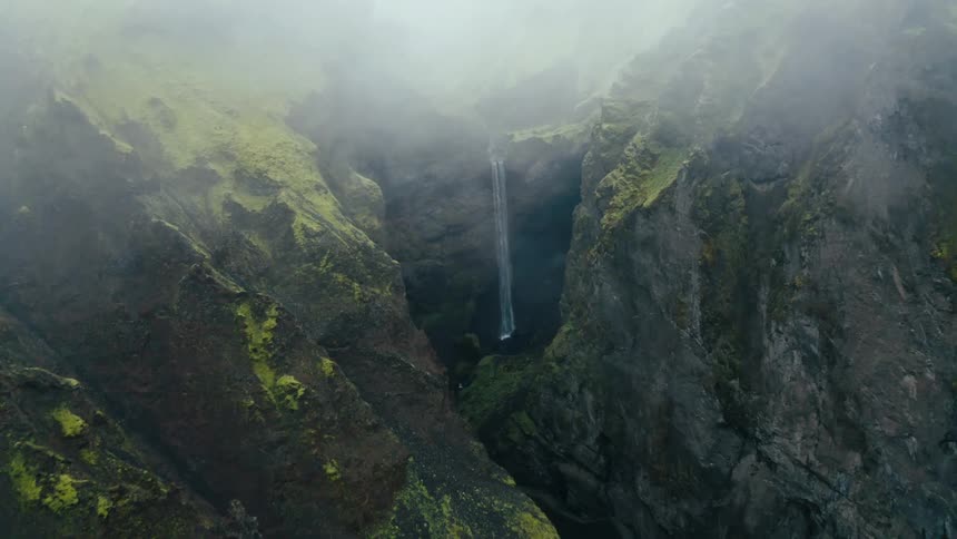 Aerial view of a waterfall amidst mountains with moss