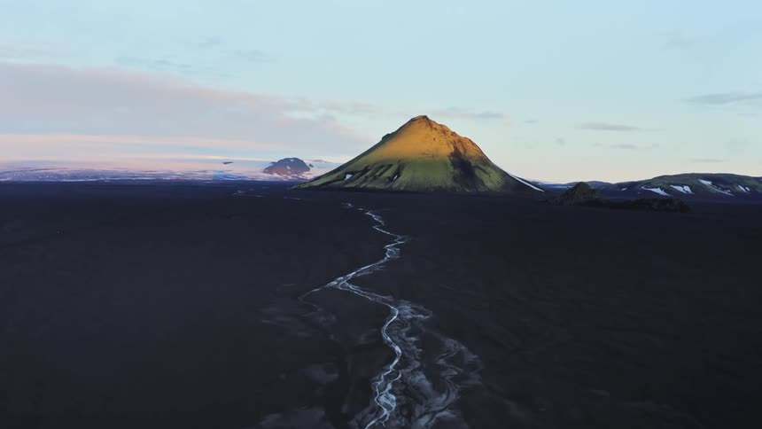 Frost covers old lava flow crossing dark ash covered plain toward volcanic mountain under a red tinted sky