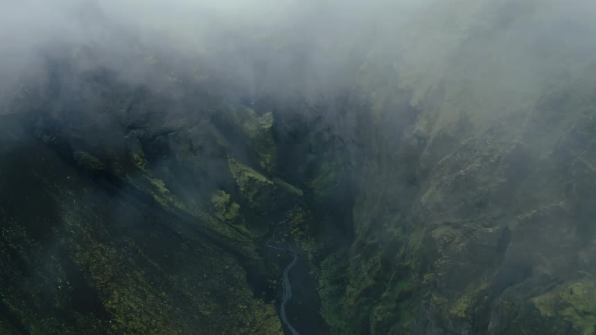 Aerial view of hidden waterfalls between mountains with moss on a foggy day