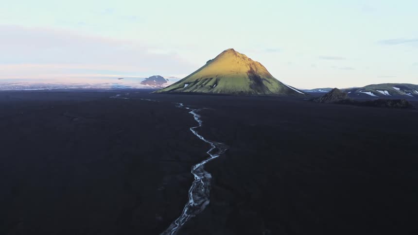 A region with black sand and a small river that goes towards a large mountain