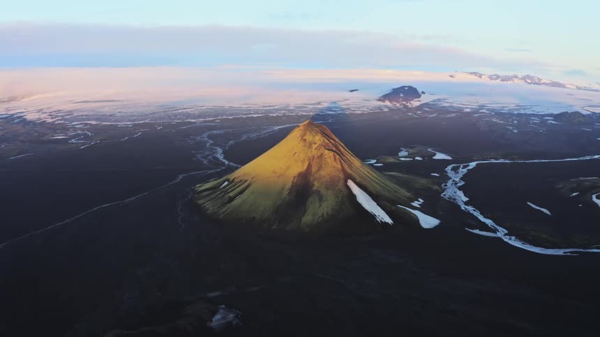 Aerial panorama of a mountain with a peak amidst black terrain and snow on a morning