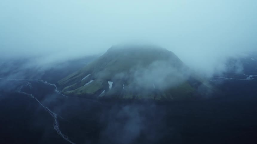 Aerial panorama of a mountain amidst black terrain on a cloudy and foggy day