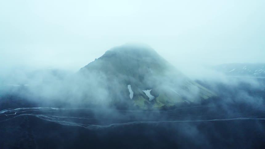 Aerial view of a volcano surrounded by black terrain on a foggy day