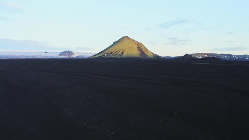 Pale yellow green mountain rises above dark soiled plain crossed by multiple frozen streams