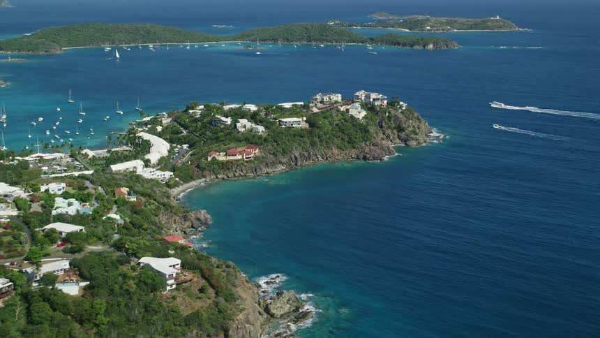 Several houses on land facing the sea with many boats sailing and many trees on the land