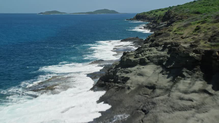 Waves crash against stony shore with multiple small islands on the horizon