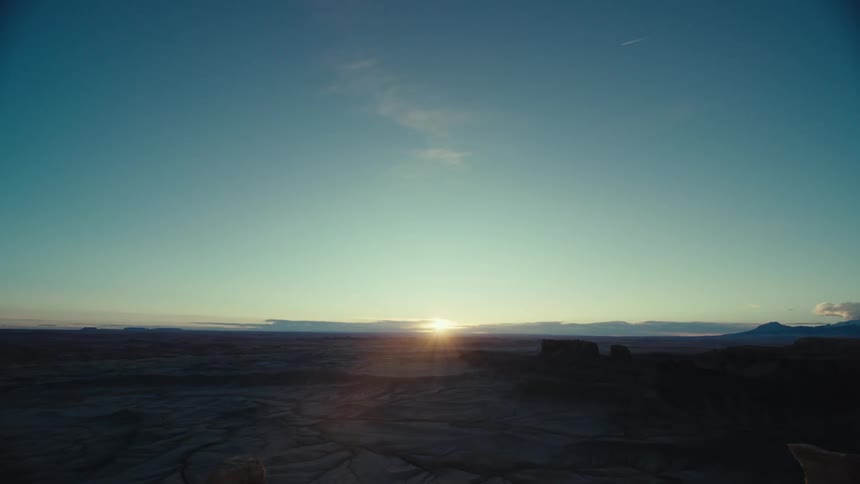 A region with rocky soil and on the horizon the sun shining in a blue sky