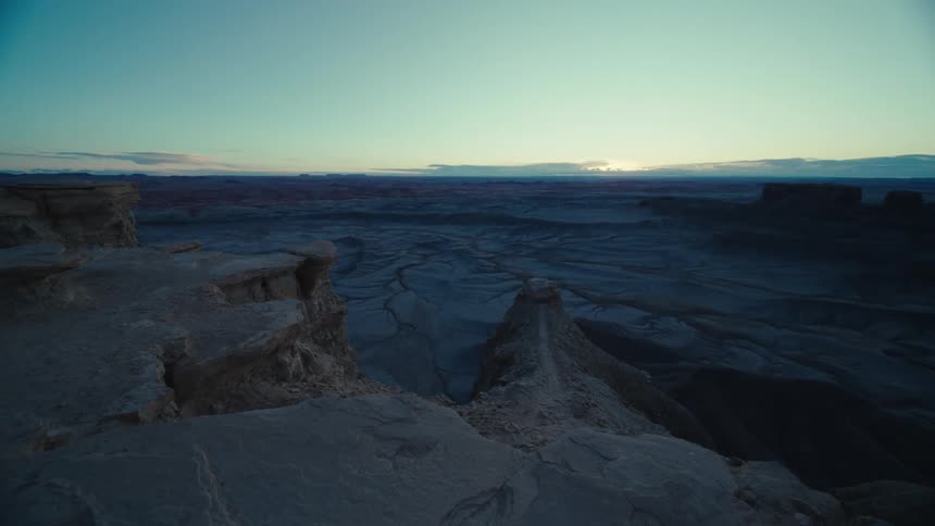 Sun brightens the horizon a considerable distance from plateaus and mesas towering over arid landscape