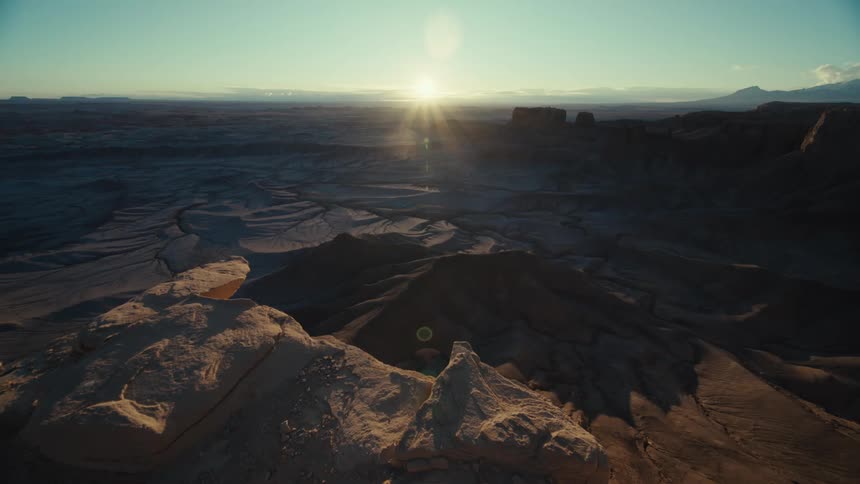 Sun shines from horizon across arid landscape containing mesas and plateaus