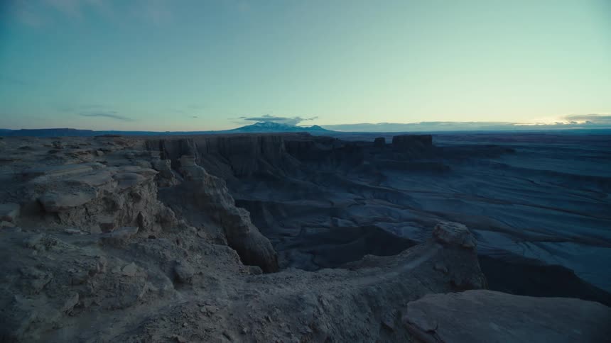 Ravine separates plateau from arid plain while sun shines on horizon
