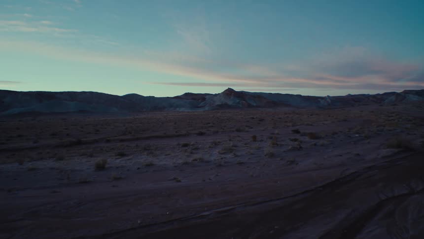 View of a desert terrain with valleys in the background under a purple dawn sky