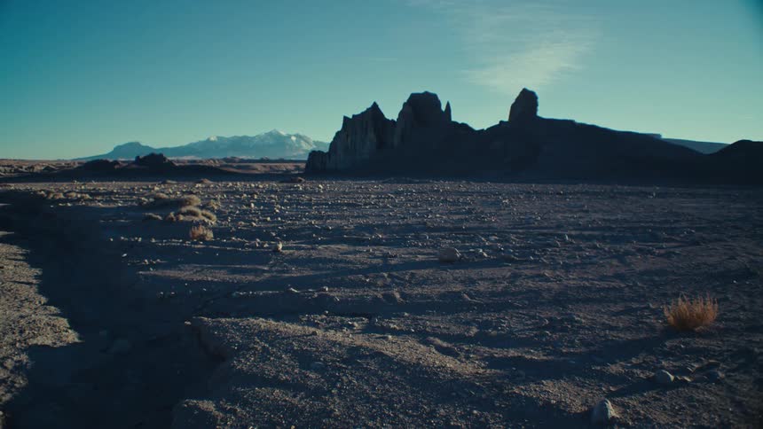 Partially silhouetted mountain and foggy mountains rise above flat arid landscape on a slightly cloudy day