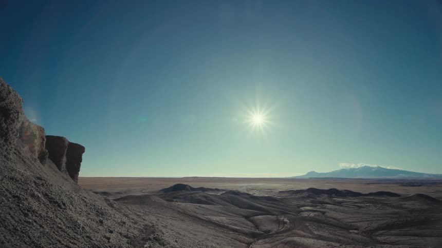 View of a desert landscape with geological rocks and the sun on the horizon in a clear blue sky
