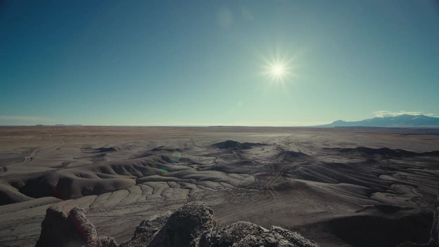 Panoramic view of a desert terrain with rocky valleys and the sun on the horizon
