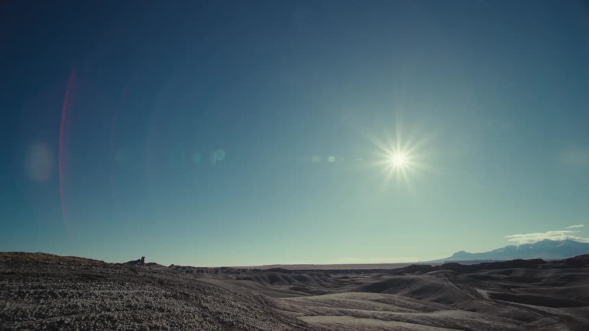Panorama of a desert terrain on a day with a blue sky with the sun reflecting and valleys on the horizon
