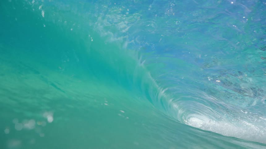 A large wave curling into a tube as it heads to shore seen from the water